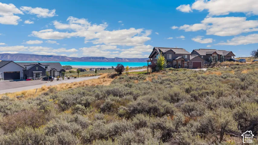 Waterfront property with mountain backdrop, featuring a multi-level home with a detached garage, and a paved driveway