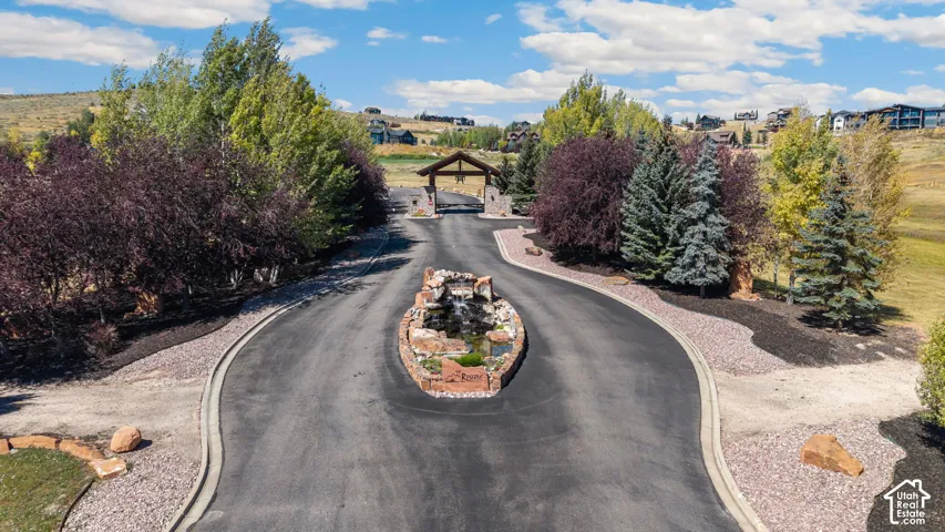Paved entry drive with a central rock water feature, surrounded by mature trees and landscaping