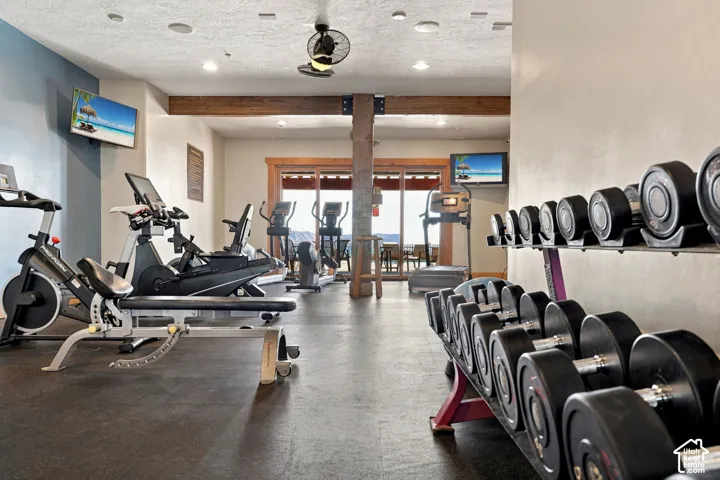Fitness area featuring rubber flooring, exposed wood beams, ceiling fan, and recessed lighting