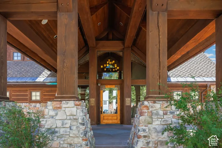 Exposed wood beam construction, stone column bases, wood-plank soffit, glass paneled entry door, and large overhead chandelier