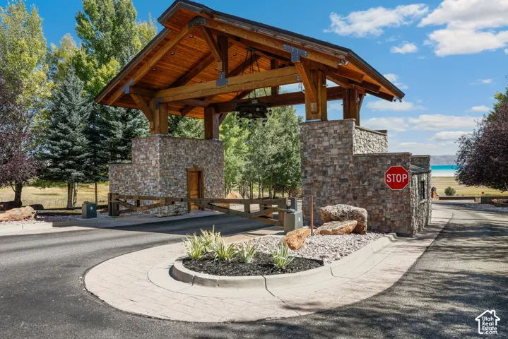 Stone and wood-beam entry structure with a natural wood gate, landscaped island, and paved access road