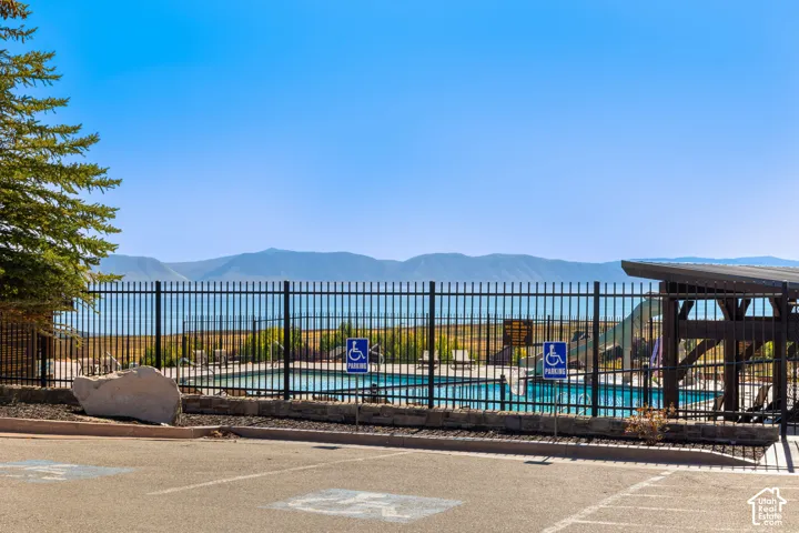 Swimming pool with surrounding fencing, adjacent covered patio structure, and a backdrop of expansive water and distant mountains