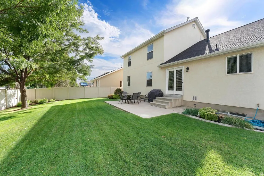 Expansive rear yard featuring a large concrete patio, manicured lawn, and mature tree