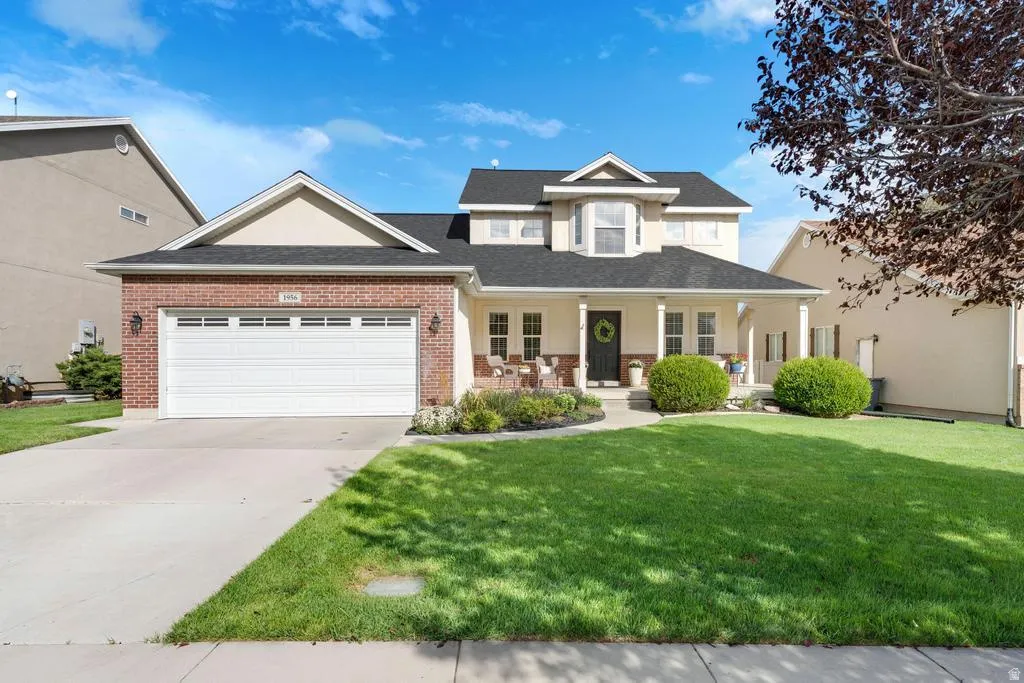 Two-story residence featuring brick and siding facade, a covered front porch with columns, a prominent bay window, an attached garage, and a concrete driveway
