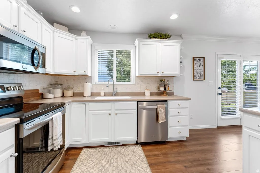 Kitchen featuring white cabinetry, stainless steel appliances, light-toned countertops, tile backsplash, and wood-finish flooring