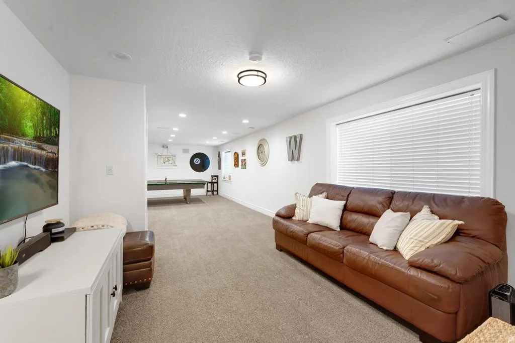 Expansive carpeted room with recessed lighting and a large window featuring blinds