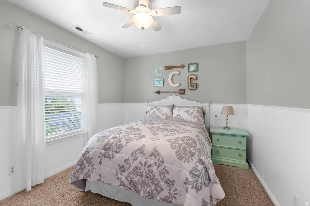 Recessed window with blinds, ceiling fan with integrated lighting, textured wall paneling, light gray painted walls, and textured carpet flooring