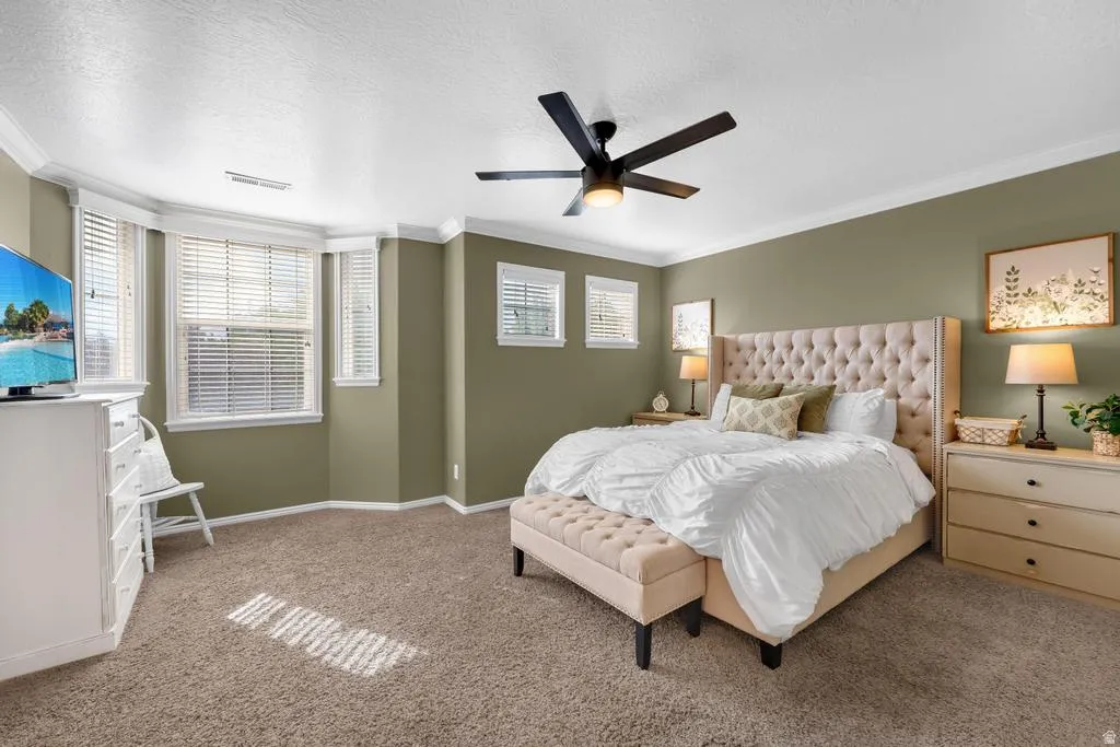 Bay window with multiple windows, crown molding, ceiling fan with integrated lighting, textured ceiling, and carpeted flooring
