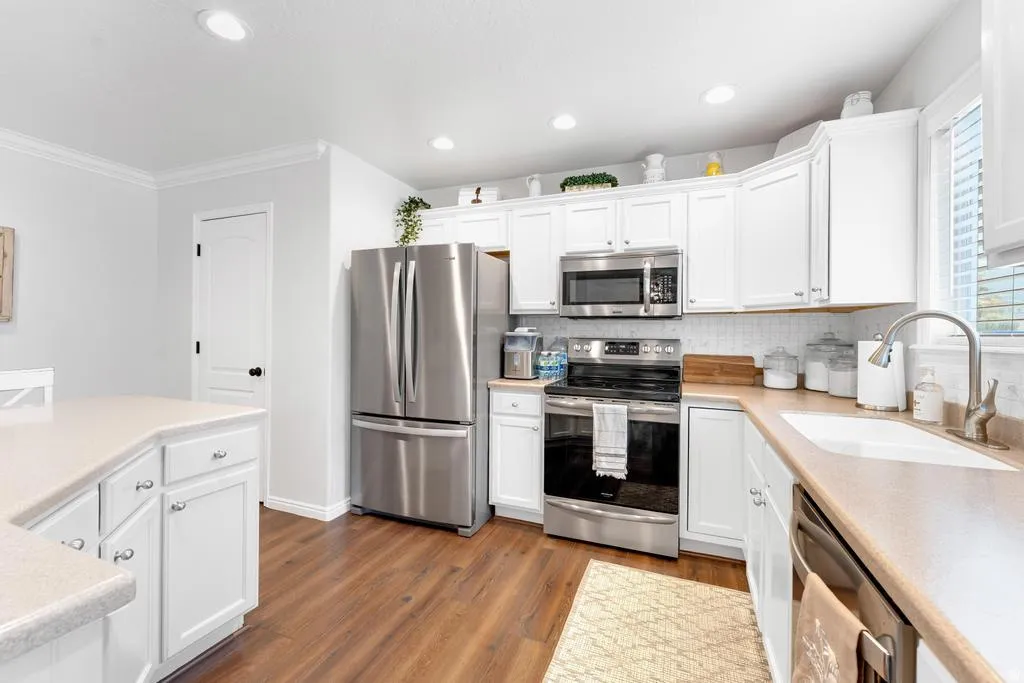 Kitchen featuring white shaker-style cabinetry, wood-finish flooring, stainless steel appliances, and a kitchen island with storage
