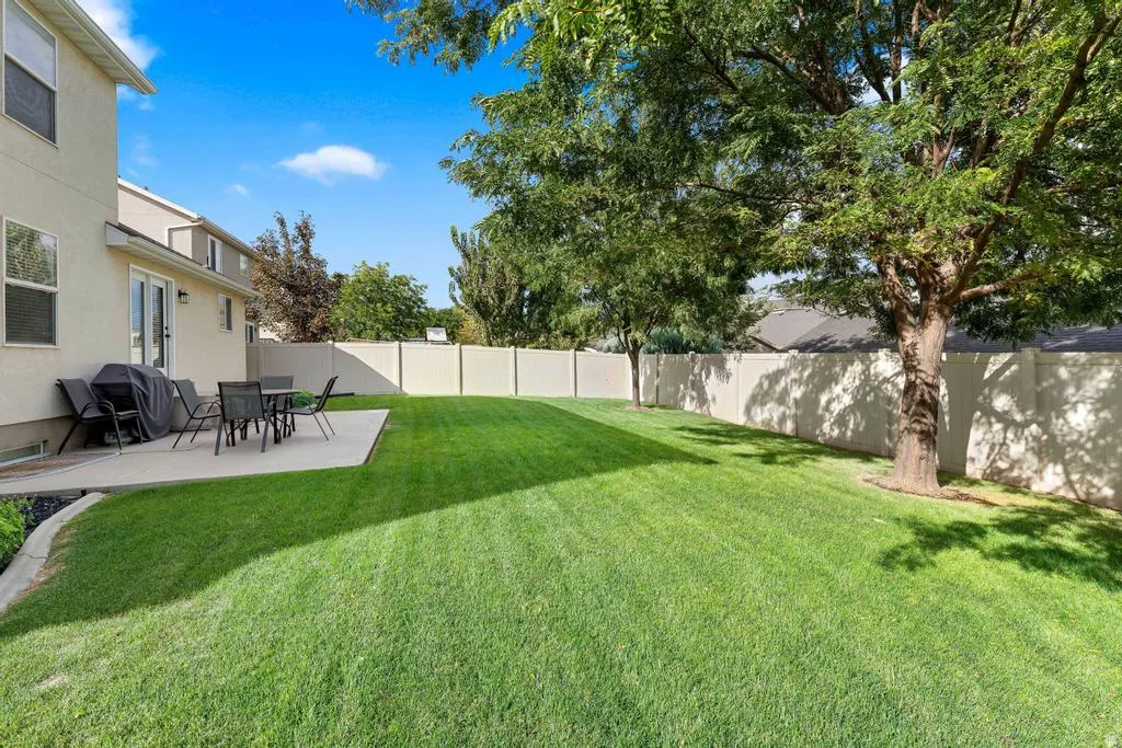 Expansive lawn area, concrete patio, mature trees, privacy fencing, and exterior double doors