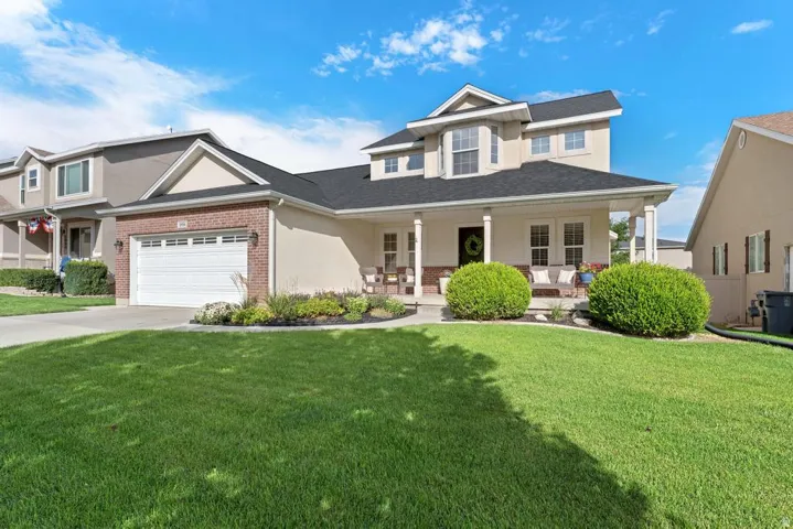 Paved driveway, attached two-car garage, covered porch with columns, brick and stucco exterior, and a dormer window