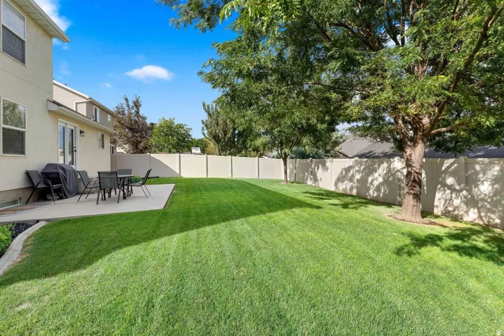 Expansive lawn area, concrete patio, mature trees, privacy fencing, and exterior double doors