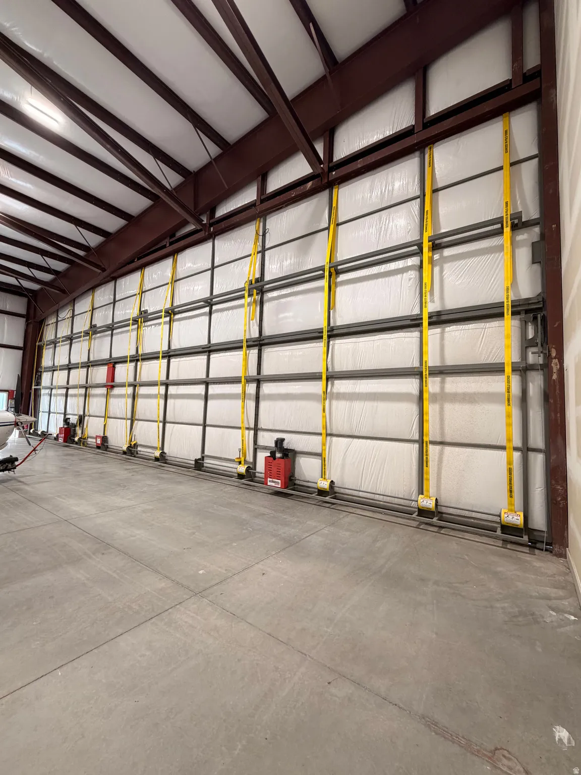 Concrete flooring with control joints, exposed metal structural beams, insulated wall panels, and a high ceiling