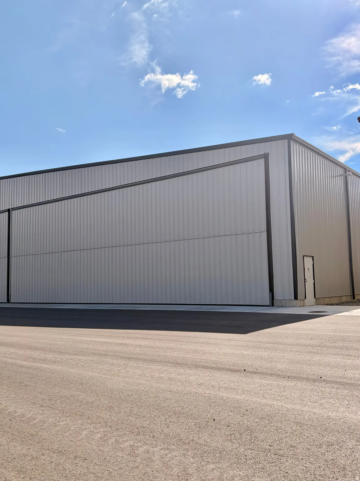 Metal-sided industrial building featuring a large hangar door, a pedestrian door, and a paved approach