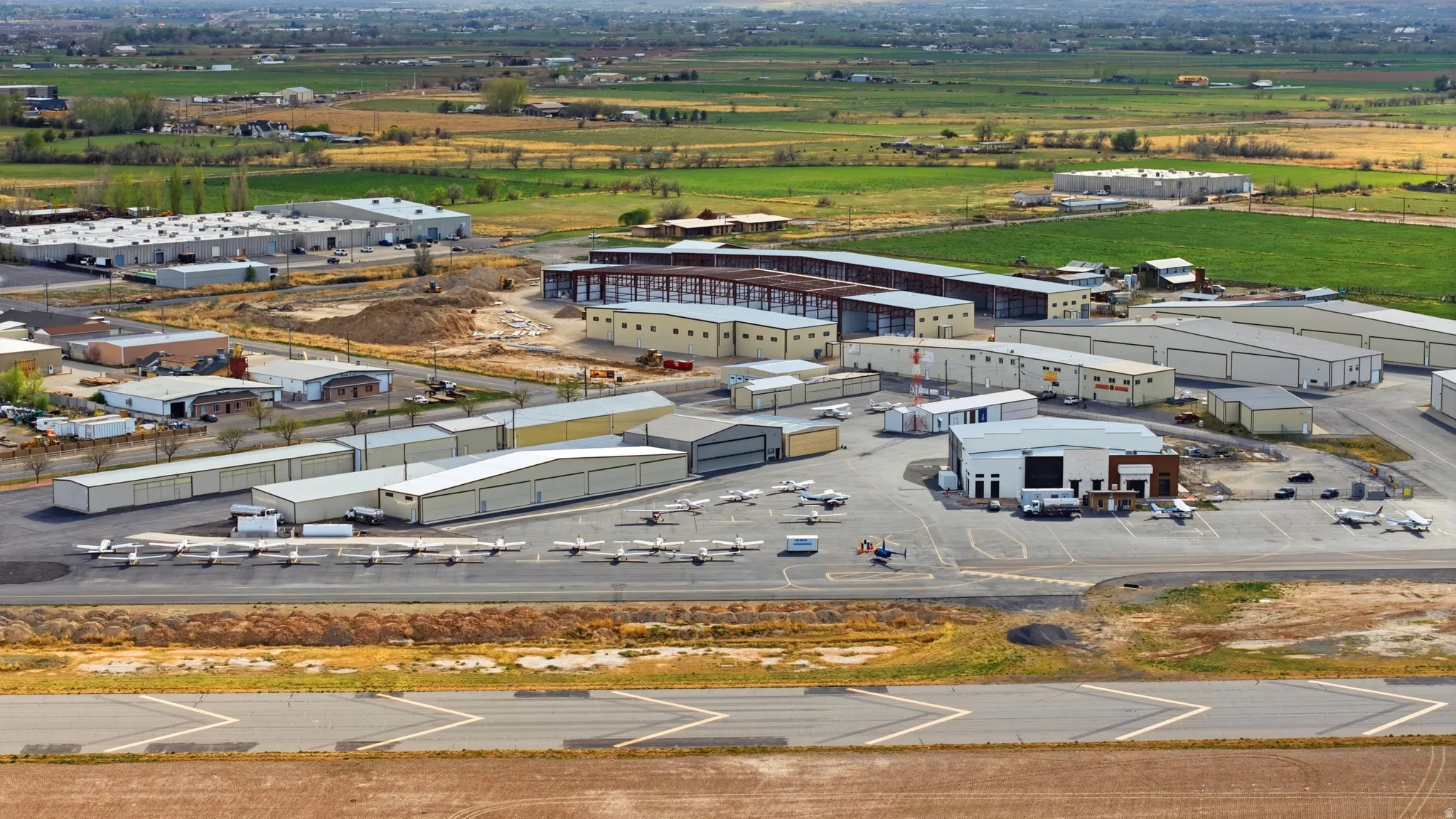 Multiple aircraft hangars, paved aircraft parking, and industrial buildings with surrounding open land