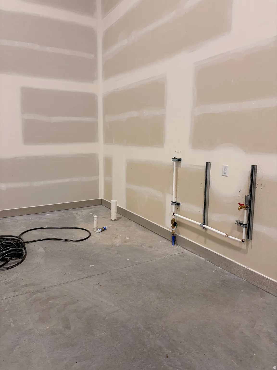 Concrete flooring, unfinished drywall, exposed plumbing, and a ground-level electrical outlet