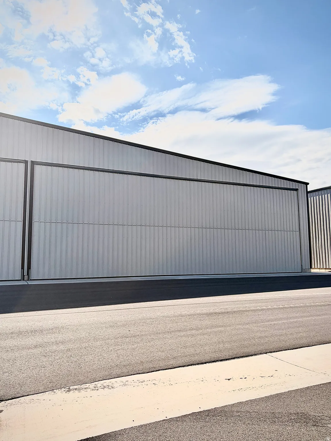 Corrugated metal siding with a dark trim, large hangar door, and paved asphalt surface