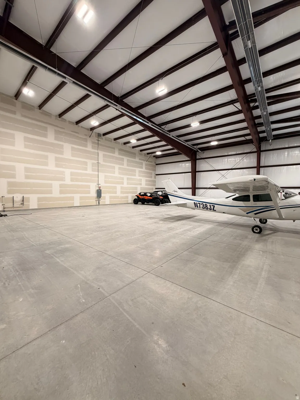 Expansive concrete flooring with a high-pitched ceiling, exposed support beams, integrated overhead lighting, and unfinished wall paneling