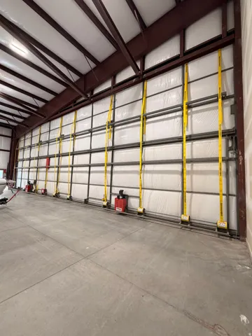 Concrete flooring with control joints, exposed metal structural beams, insulated wall panels, and a high ceiling