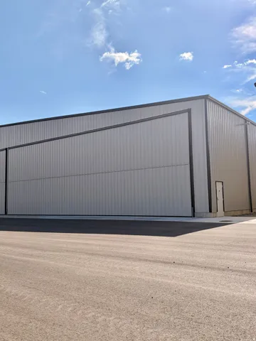 Metal-sided industrial building featuring a large hangar door, a pedestrian door, and a paved approach