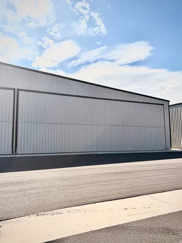Corrugated metal siding with a dark trim, large hangar door, and paved asphalt surface