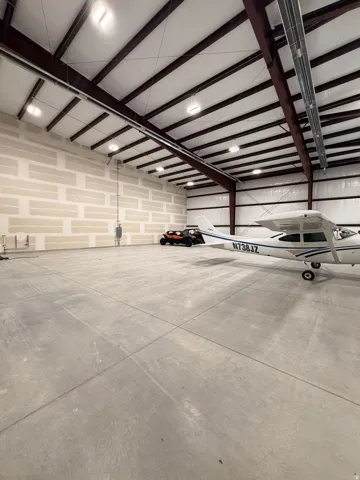 Expansive concrete flooring with a high-pitched ceiling, exposed support beams, integrated overhead lighting, and unfinished wall paneling
