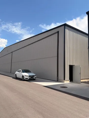 Metal panel exterior, black trimmed roofline, large sliding bay doors, concrete entry pad, and single entry door