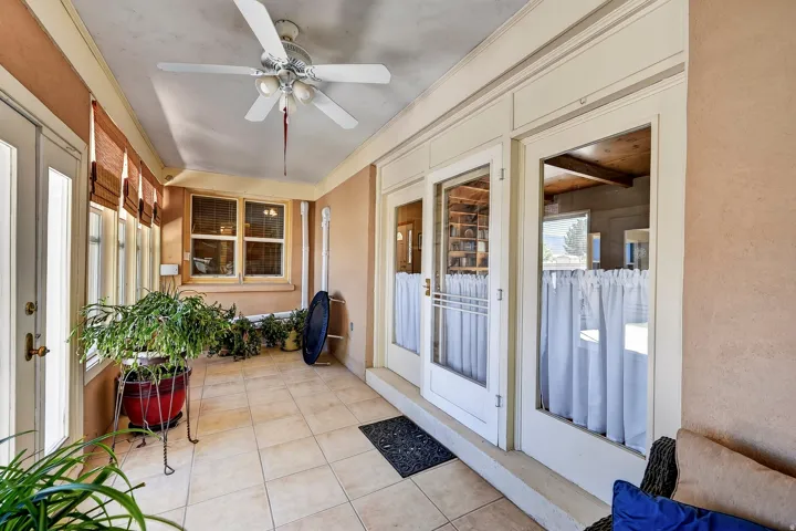 Enclosed porch featuring a ceiling fan with light kit, tiled flooring, multiple windows with blinds, and glass-paneled doors