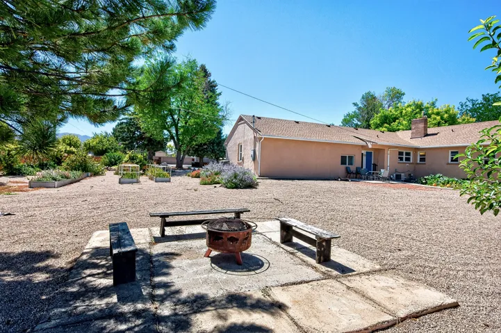 Spacious gravel yard with multiple raised garden beds, a dedicated fire pit area, and a stucco exterior with a durable shingle roof