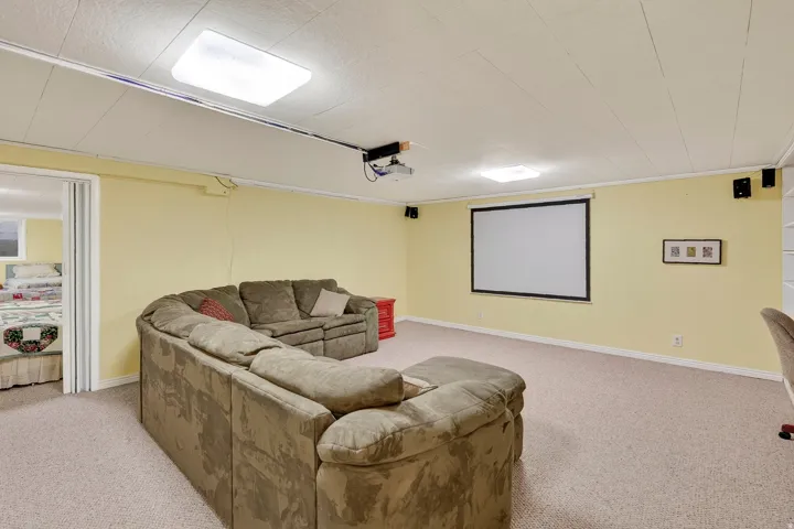 Recessed projector screen, ceiling-mounted projector, wall-mounted speakers, drop ceiling with integrated lighting, and neutral carpeting
