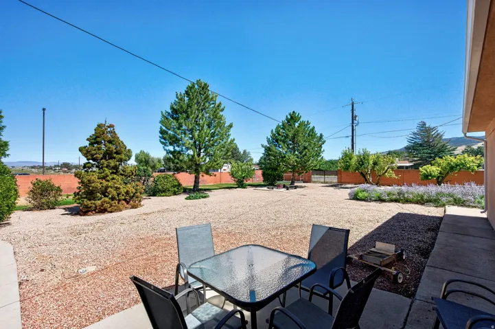 Expansive gravel yard with mature trees, shrubbery, and a decorative floral bed