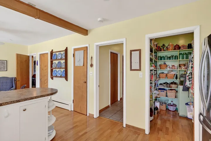 Hardwood flooring throughout, kitchen island with counter seating, exposed wood beam, and a spacious pantry with shelving