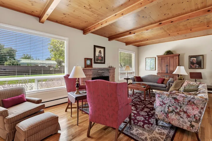 Wood-finish flooring, exposed wood beam ceiling, expansive windows, and a stone-faced fireplace