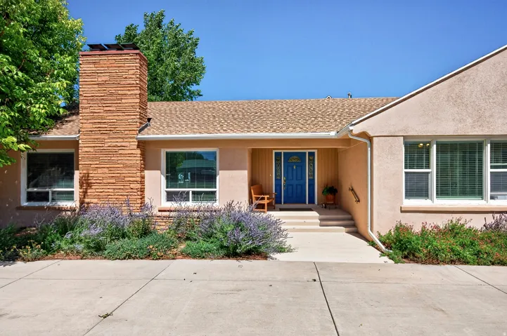 Stucco exterior with a prominent brick chimney, asphalt shingle roofing, and a vibrant blue entry door