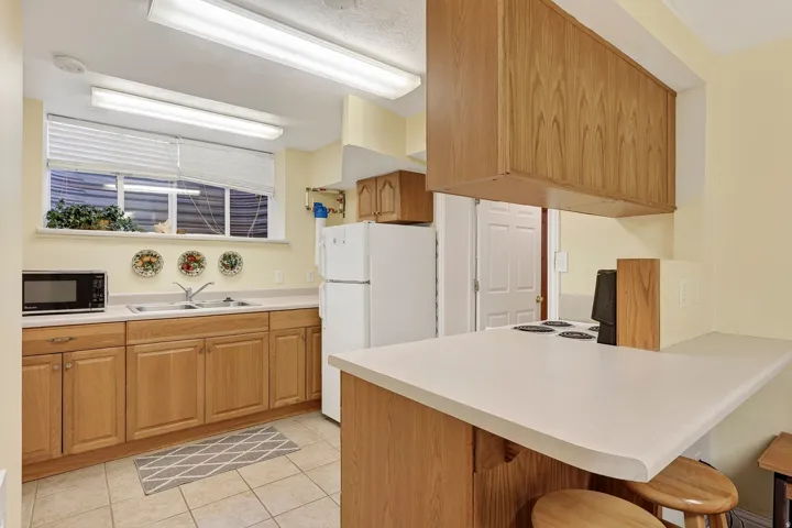 Light wood-finish cabinetry, solid surface countertops, tiled flooring, and a stainless steel sink with a dual faucet
