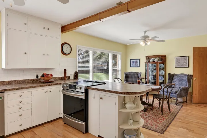 White cabinetry with brushed nickel hardware, stainless steel range, white subway tile backsplash, laminate countertops, and wood-finish flooring