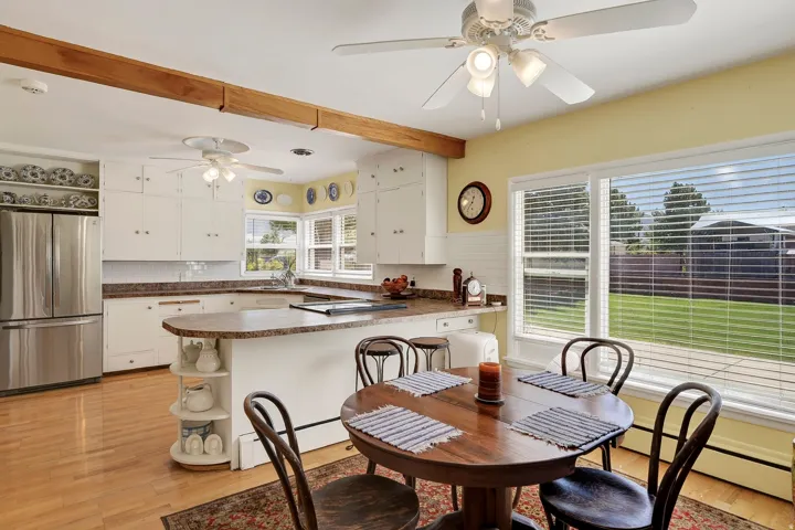 White cabinetry, stainless steel refrigerator, wood-finish flooring, wood beam accent, and a large window
