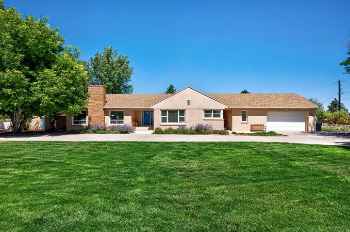 Expansive front lawn, stucco exterior, brick chimney, attached garage, and mature landscaping