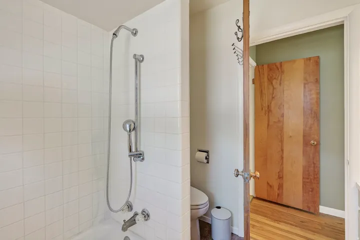 White tiled shower with a handheld shower fixture