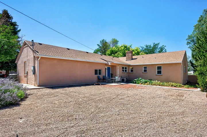 Expansive gravel yard with stucco exterior, a patio area, and mature perimeter trees