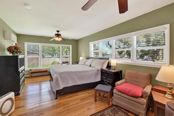 Hardwood flooring throughout, multiple windows, ceiling fans, and a wall-mounted climate control unit