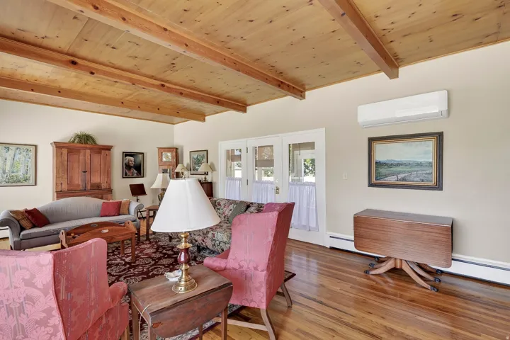 Wood-finish flooring, exposed wood beam ceiling, white walls, and white French doors