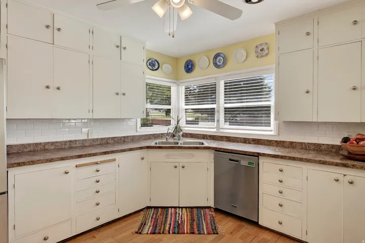 White cabinetry with ample storage, stainless steel dishwasher, double-basin sink, and corner windows