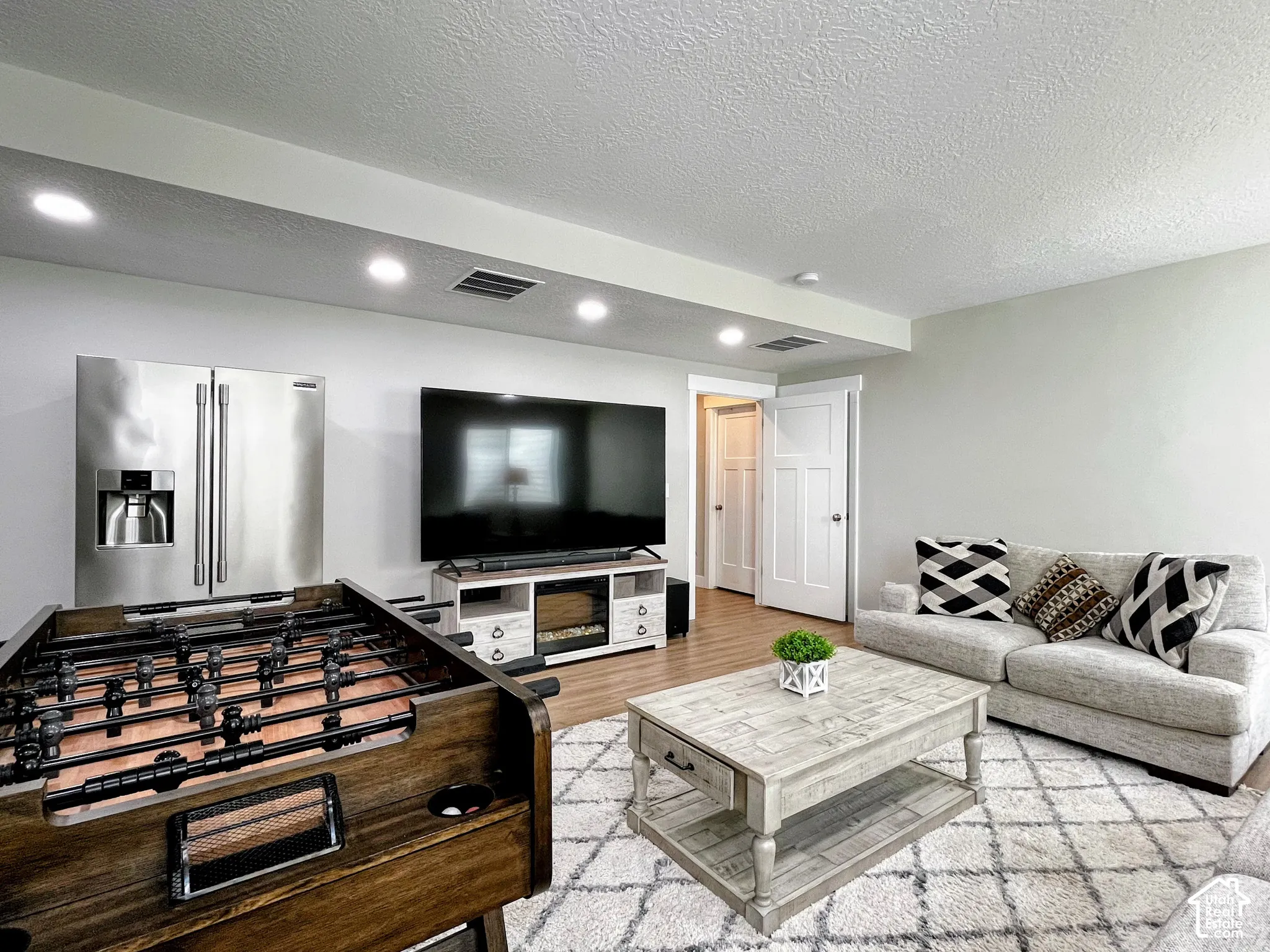 Recessed lighting illuminates the space, featuring a stainless steel refrigerator and wood-finish flooring