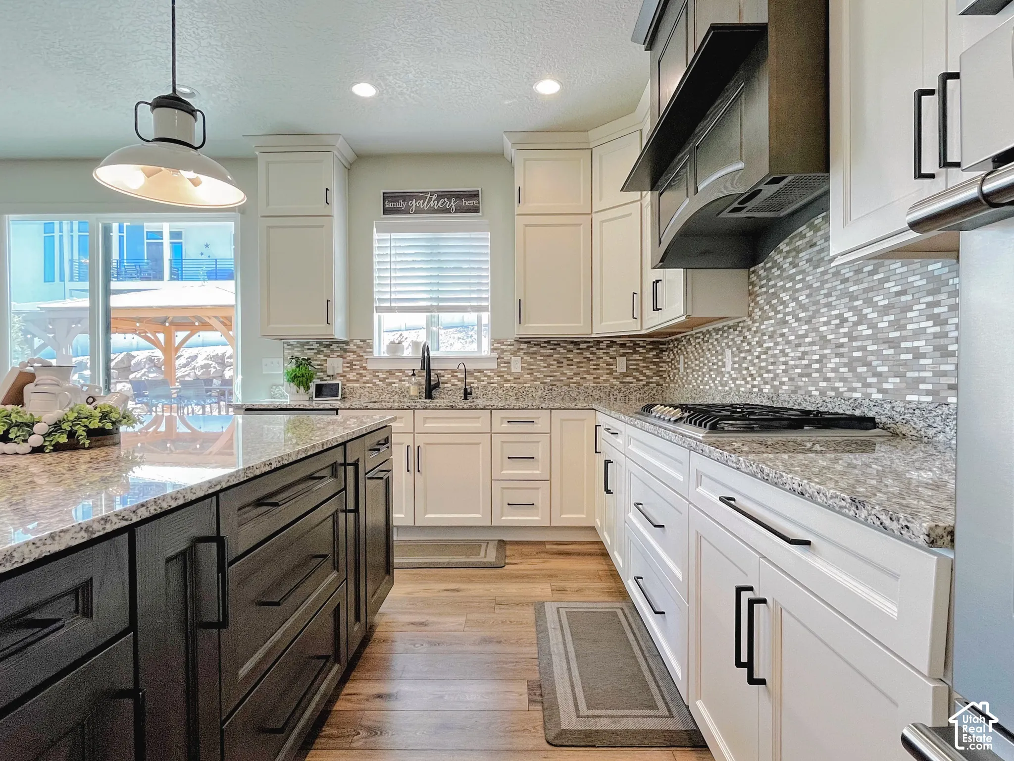 Kitchen featuring white cabinetry, a dark-toned island, light-toned countertops, a patterned tile backsplash, and wood-finish flooring