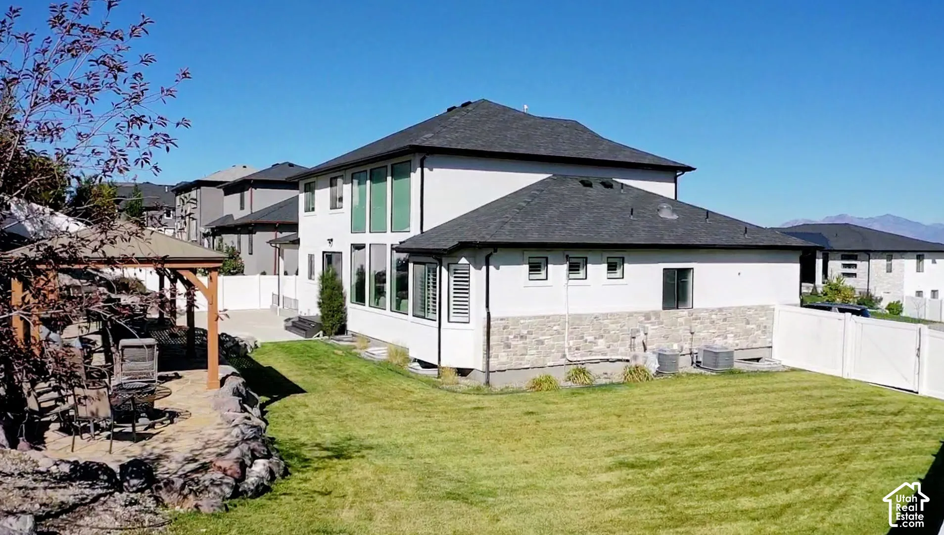 Expansive backyard featuring a manicured lawn, stone retaining walls, a wood-frame gazebo, and a privacy fence