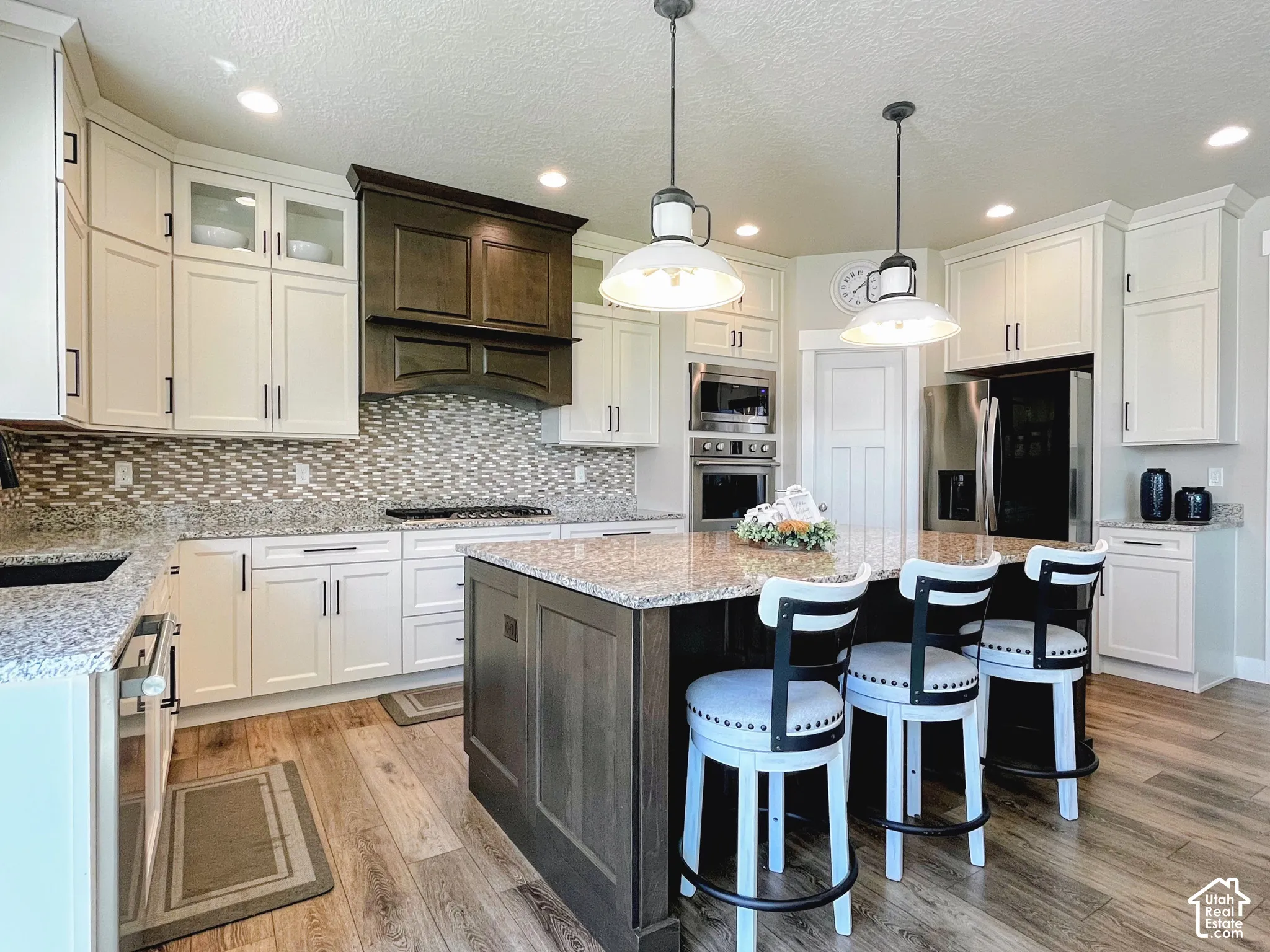 Wood-finish flooring leading to a kitchen with white cabinetry, a dark wood-stained island with a granite countertop, and stainless steel appliances
