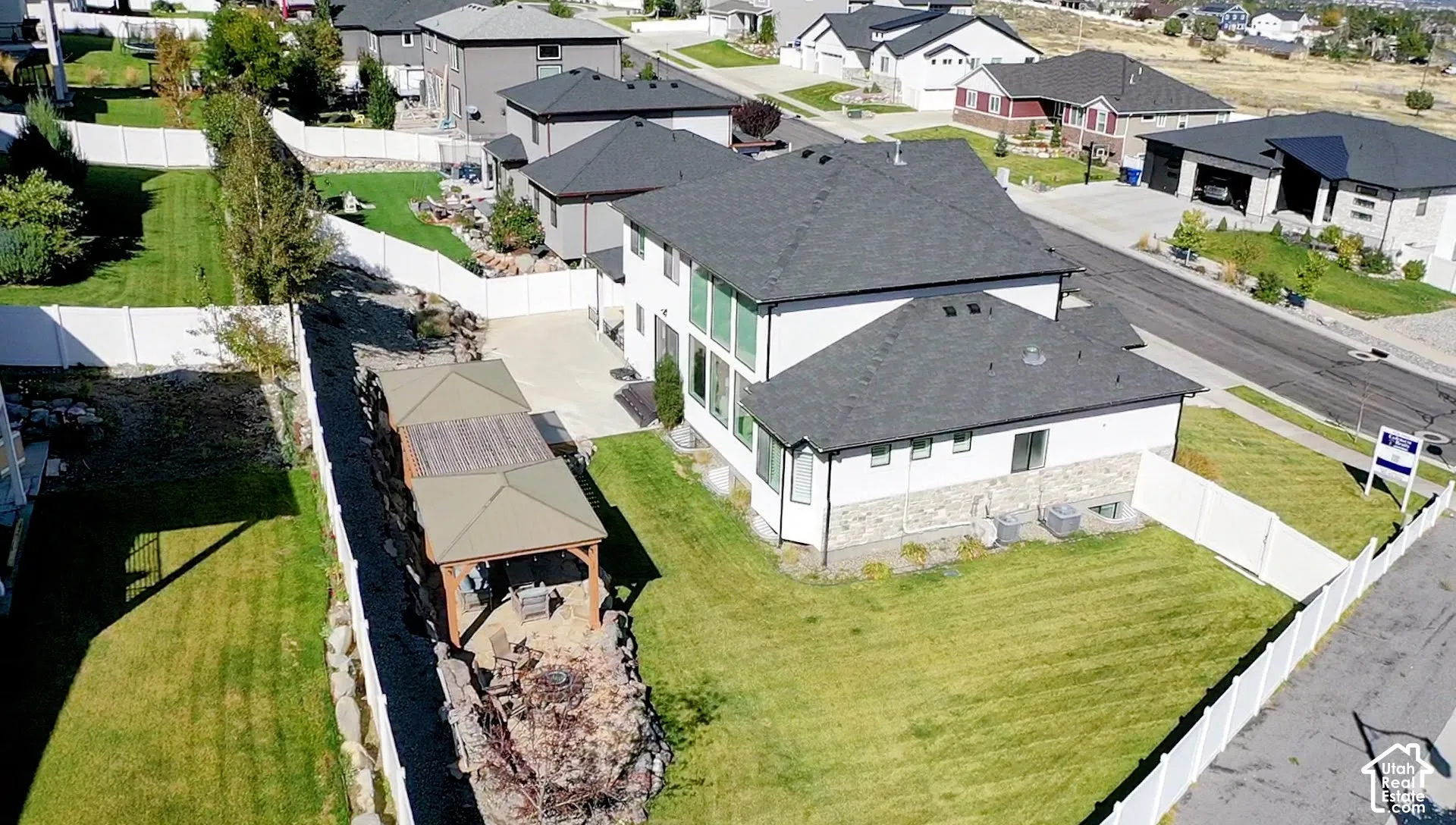 Expansive backyard featuring a manicured lawn, established landscaping, and a covered outdoor living area with a built-in fire pit