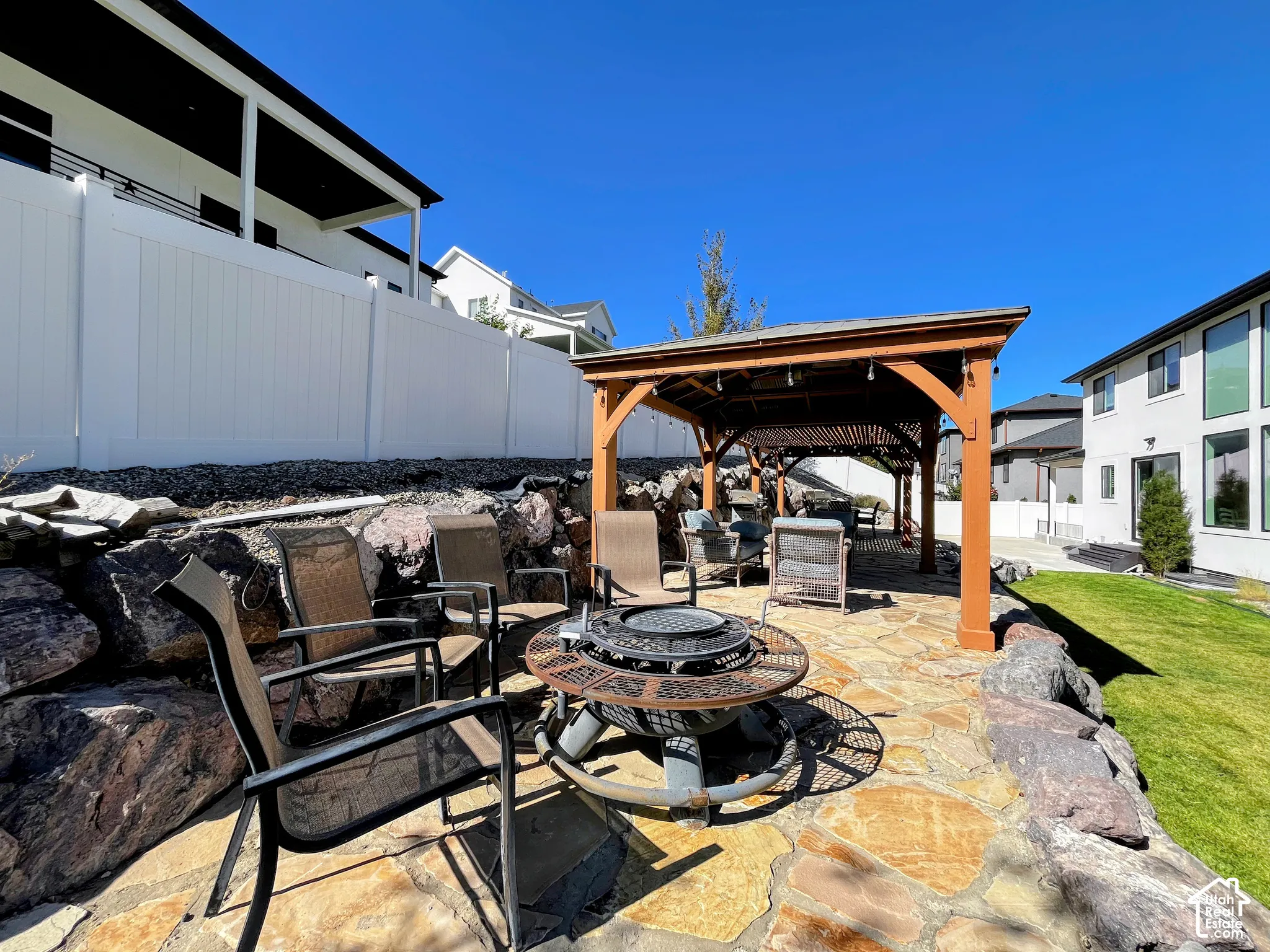 Expansive flagstone patio with a built-in fire pit, covered gazebo, and a retaining wall featuring natural stone