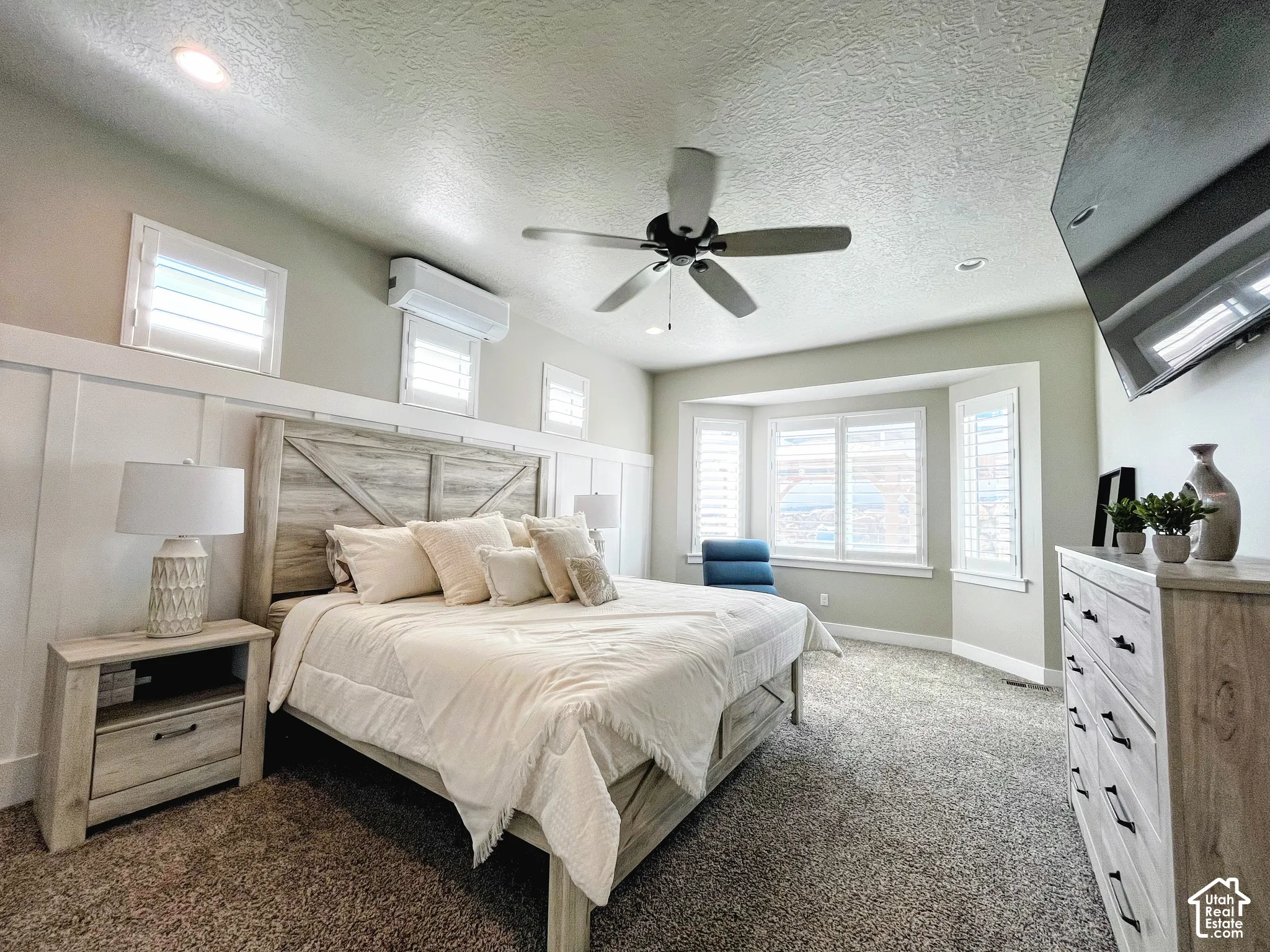 Bay window with white plantation shutters, wood-finish board and batten wall accent, recessed lighting, ceiling fan, and wall-mounted air conditioning unit